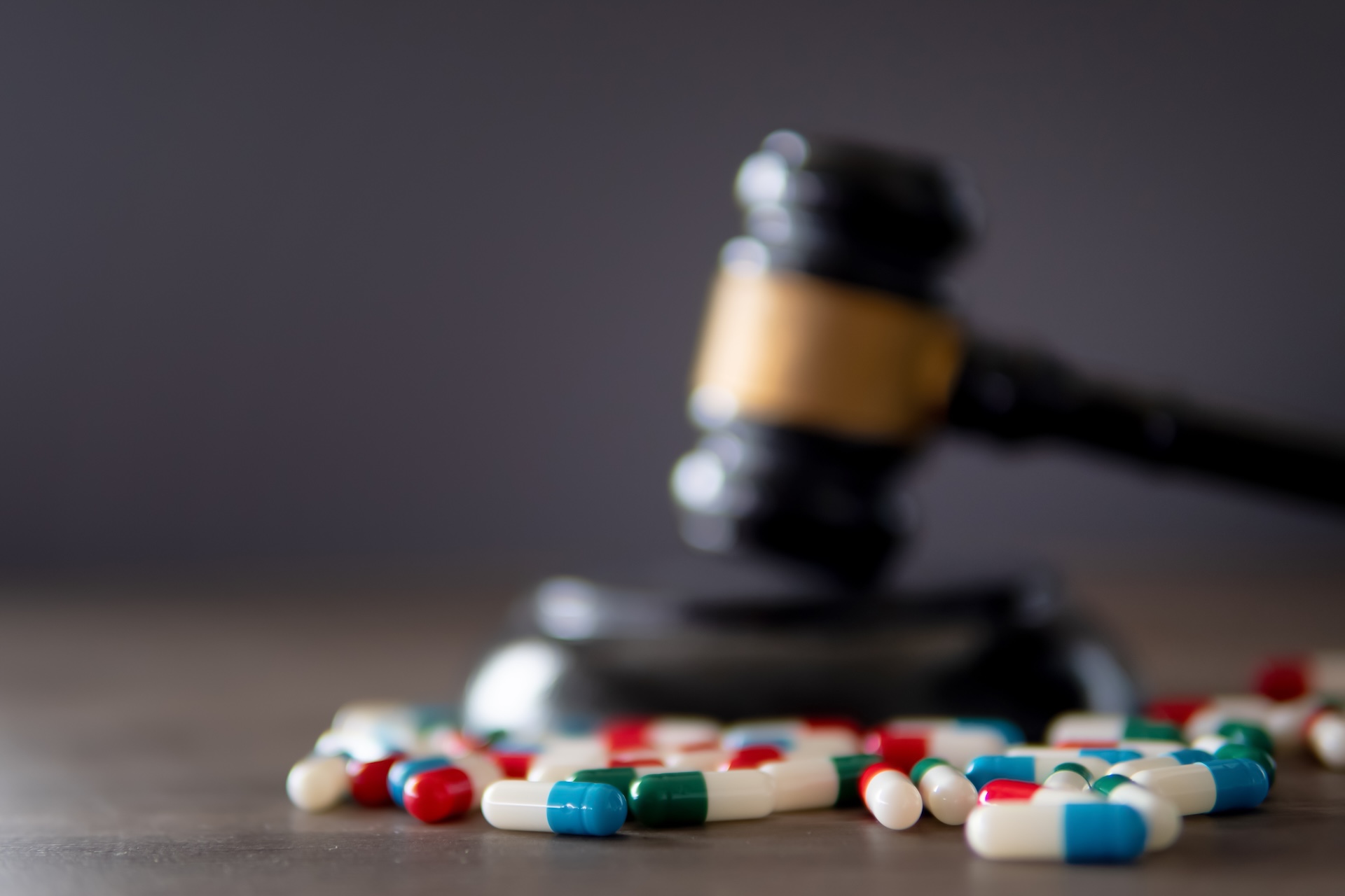 A judge’s gavel resting on its base with various colorful pills and capsules scattered in the foreground, symbolizing legal issues related to medication or pharmaceuticals.
