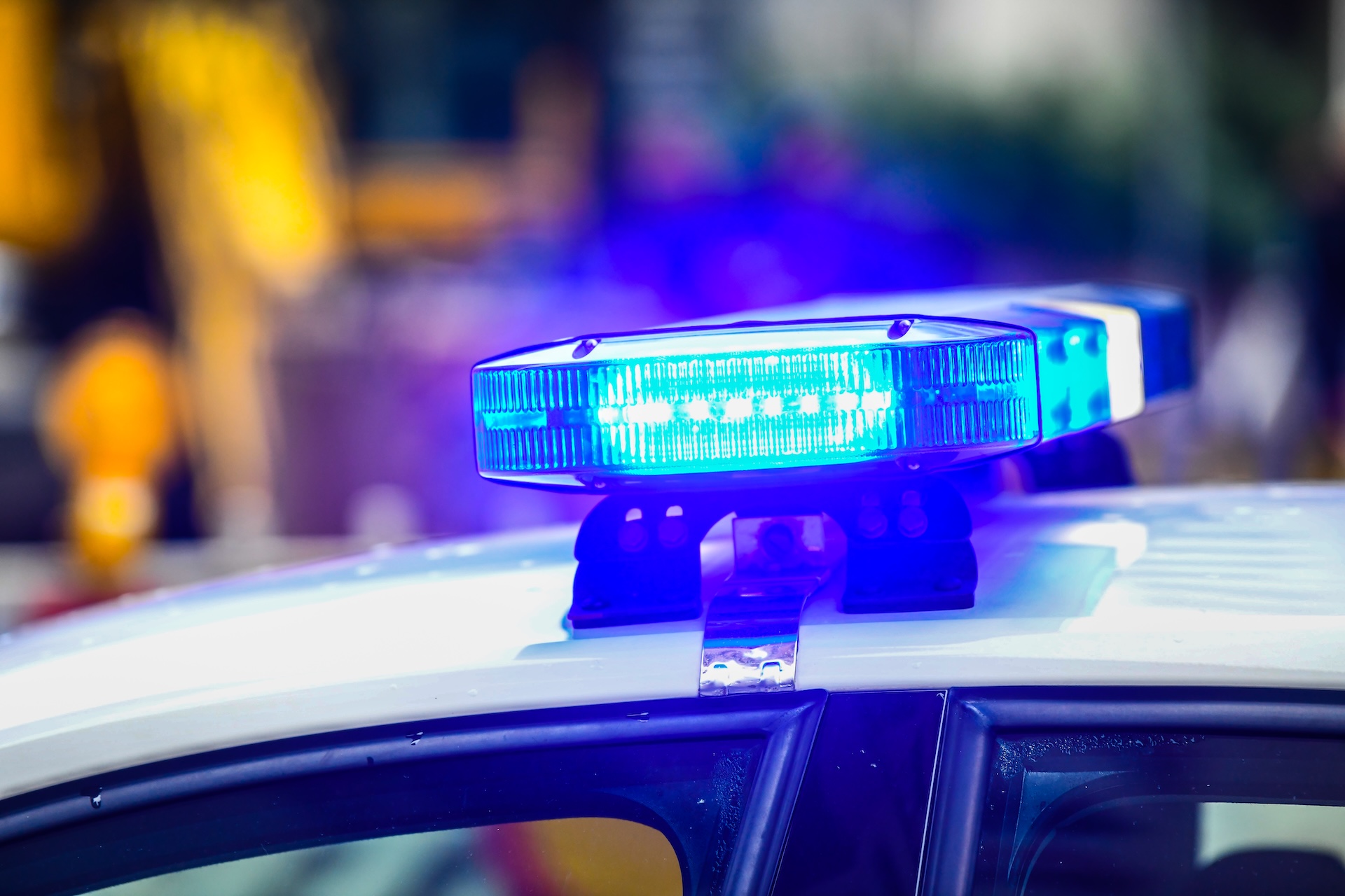 Close-up of a blue emergency police siren light flashing on top of a white police car, with a blurred background of outdoor surroundings.