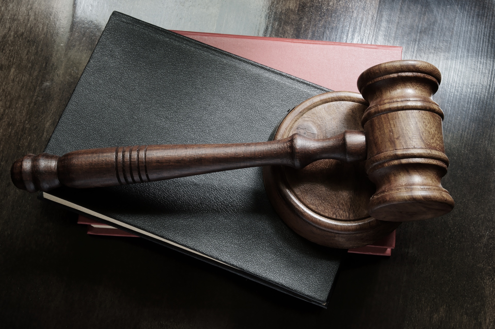 A wooden gavel rests on its sound block atop two closed hardcover books with dark and red covers, placed on a dark wooden surface—reminiscent of those found in Walker County courts Huntsville.