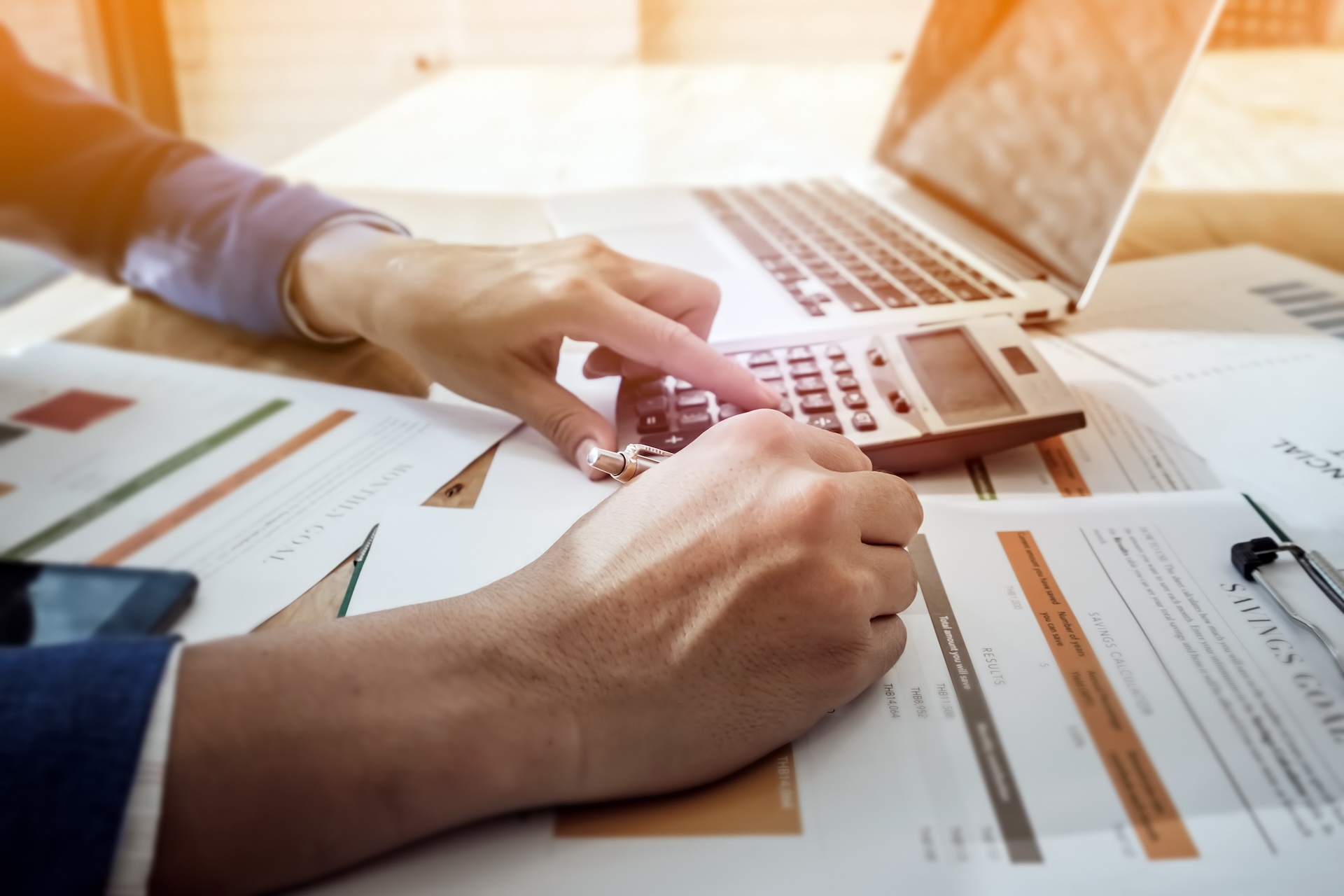 Hands using a calculator beside household bills and financial paperwork. Hands using a calculator beside household bills and financial paperwork.