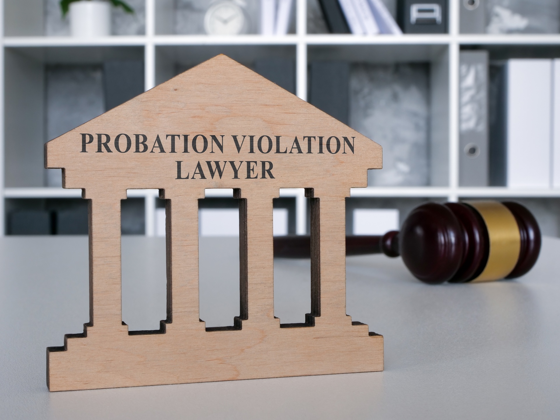 A wooden courthouse-shaped sign reads "Probation Violation Lawyer" on a desk, with a judge’s gavel in the background and shelves filled with books and folders behind, reflecting expertise in probation violation Texas cases.