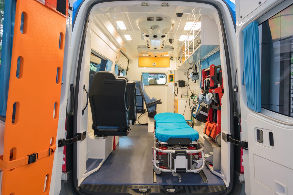 The interior of an ambulance with its rear doors open, showing the stretcher and emergency medical equipment inside.