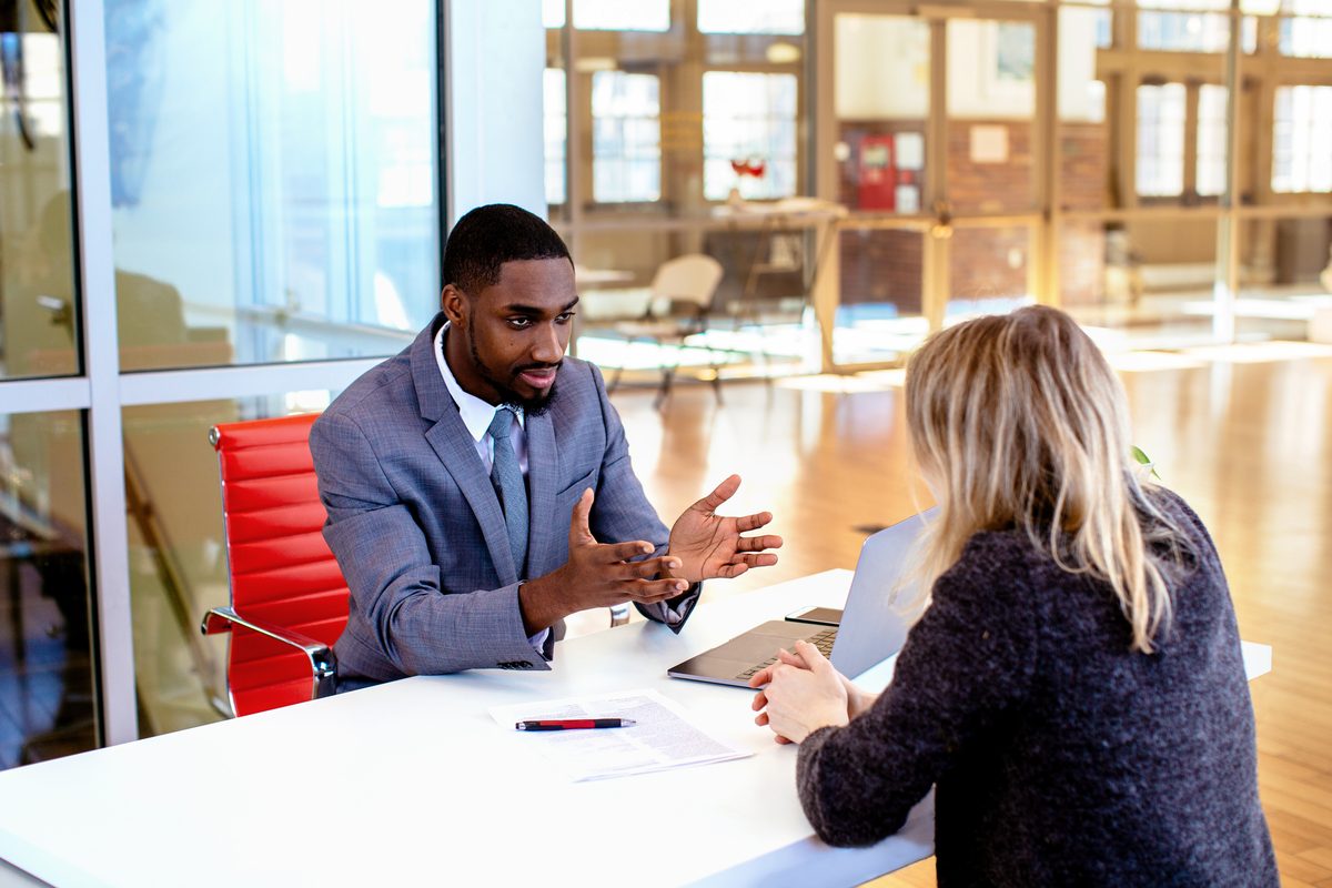 An attorney seated across a conference table explaining the terms of an agreement to a client in a bright office. An attorney seated across a conference table explaining the terms of an agreement to a client in a bright office.