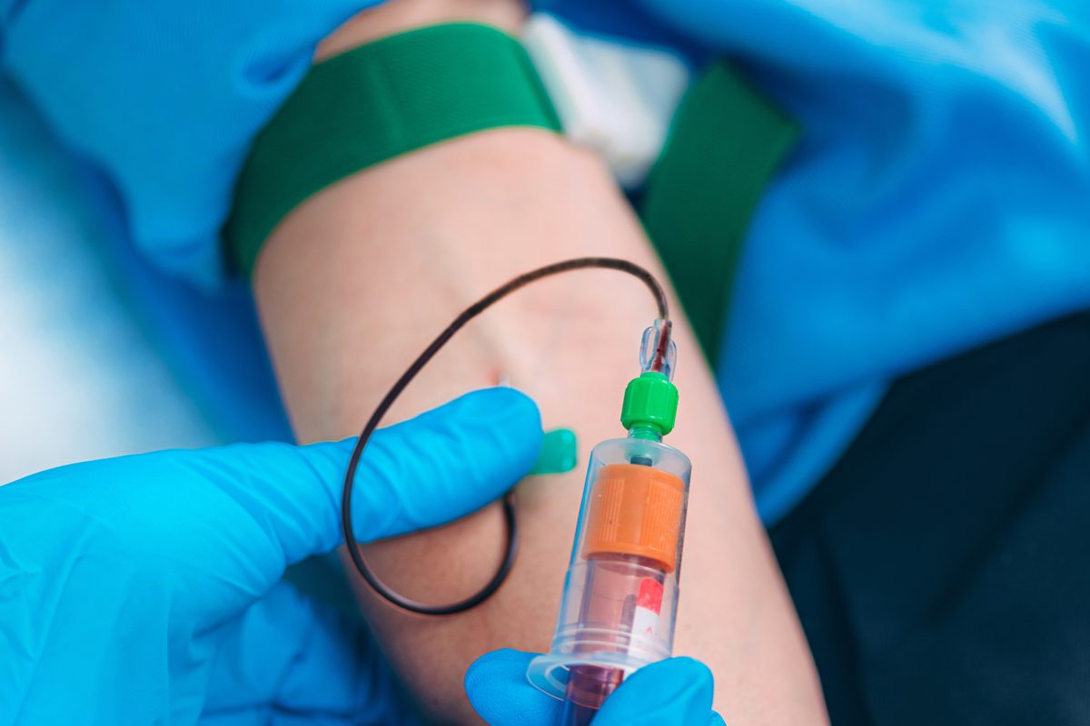 Close-up of a phlebotomist in blue gloves drawing a blood sample from a patient's arm with a tourniquet in place. Close-up of a phlebotomist in blue gloves drawing a blood sample from a patient's arm with a tourniquet in place.