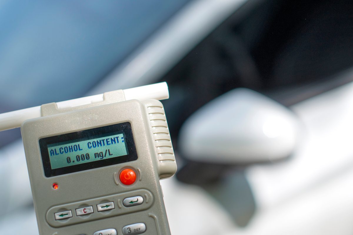 Close-up of a breath alcohol testing instrument displaying a reading of 0.000 mg/L, with a white car visible in the blurred background. Close-up of a breath alcohol testing instrument displaying a reading of 0.000 mg/L, with a white car visible in the blurred background.