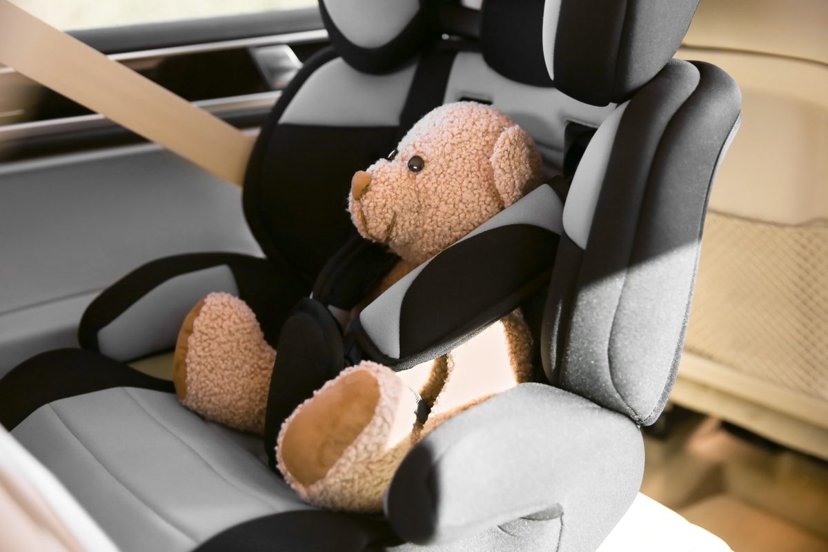 An empty child safety seat buckled into the back seat of a car with a teddy bear secured in the harness.
