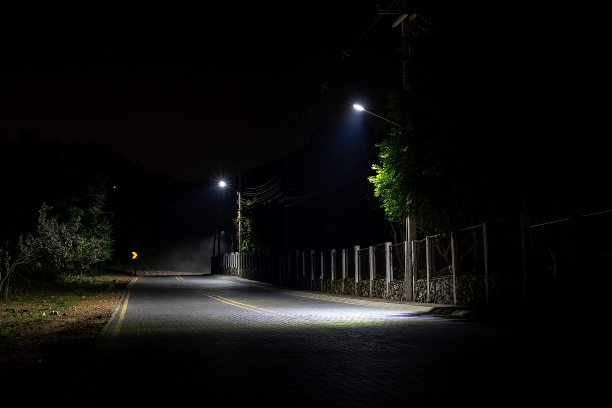 An empty two-lane road at night lit only by headlights and a single overhead street lamp. An empty two-lane road at night lit only by headlights and a single overhead street lamp.