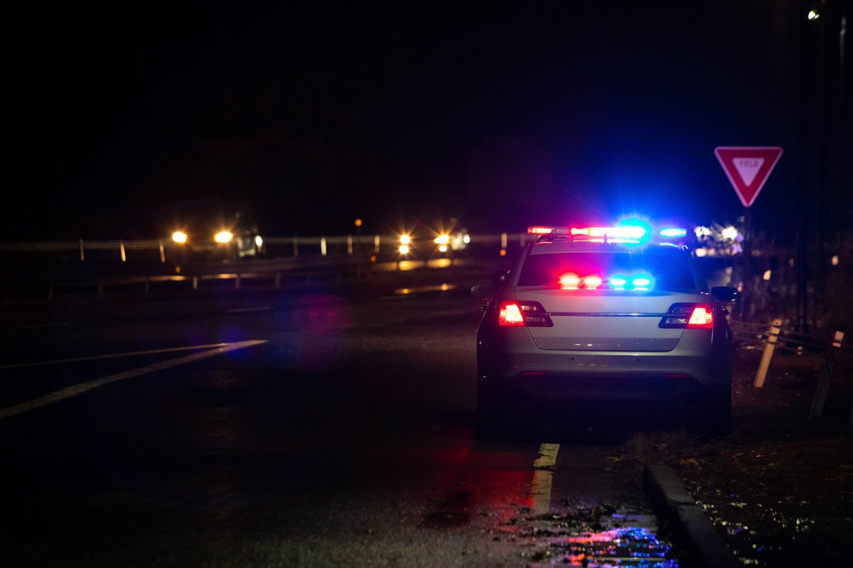A police car with red and blue emergency lights flashing during a nighttime traffic stop on a dark highway. A police car with red and blue emergency lights flashing during a nighttime traffic stop on a dark highway.