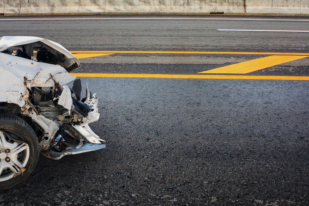 A severely damaged white car with a crushed front end stopped on a highway after a serious collision.