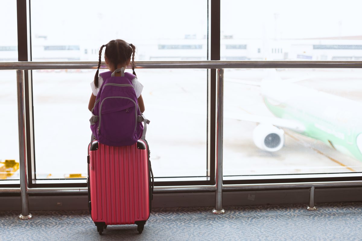 A child pulling a suitcase through an airport terminal beside a tall window.