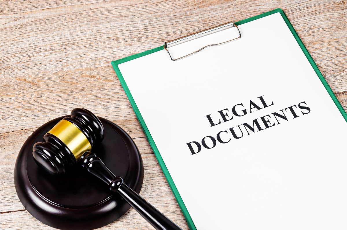 A clipboard of legal documents on a desk beside a wooden gavel. A clipboard of legal documents on a desk beside a wooden gavel.
