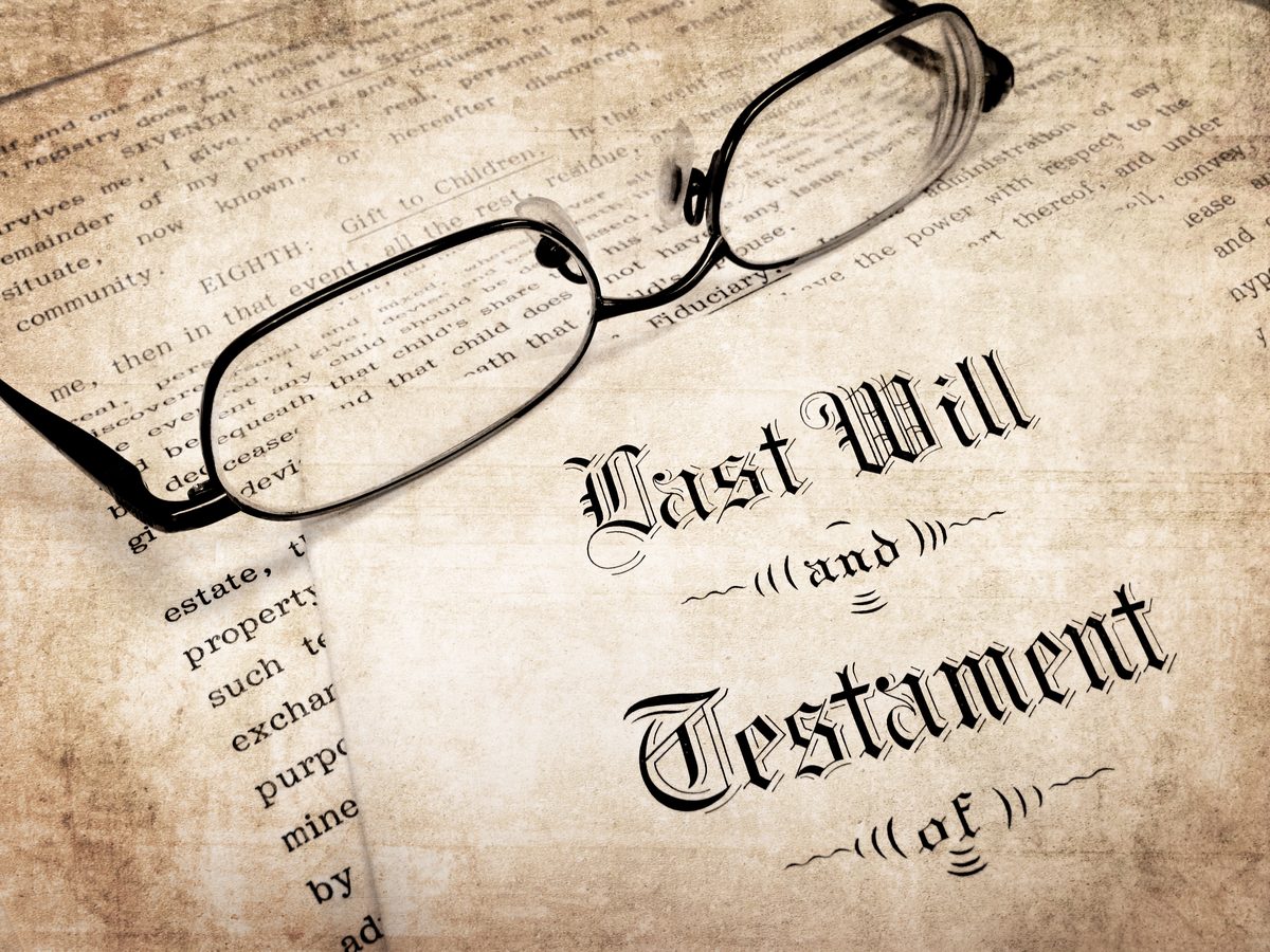 A last will and testament document resting on a desk beside a pair of reading glasses. A last will and testament document resting on a desk beside a pair of reading glasses.