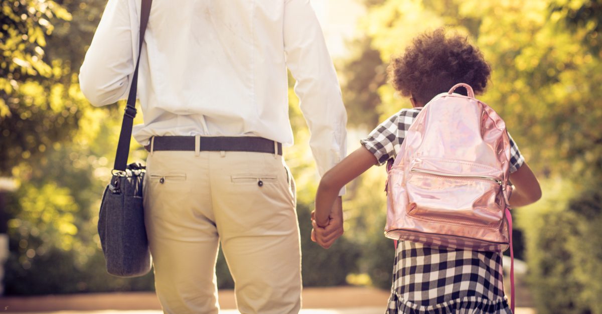 A parent and a child wearing a school backpack walking together outdoors.