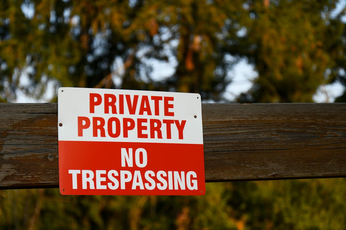 Private property no trespassing sign posted on a wooden fence along a rural hunting tract