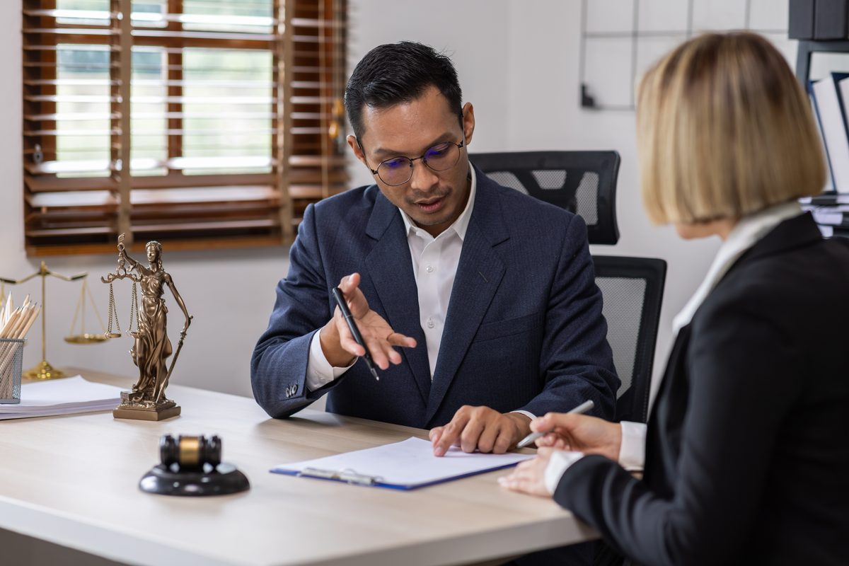 A defense attorney explains options to a client across a desk with a gavel and scales of justice A defense attorney explains options to a client across a desk with a gavel and scales of justice