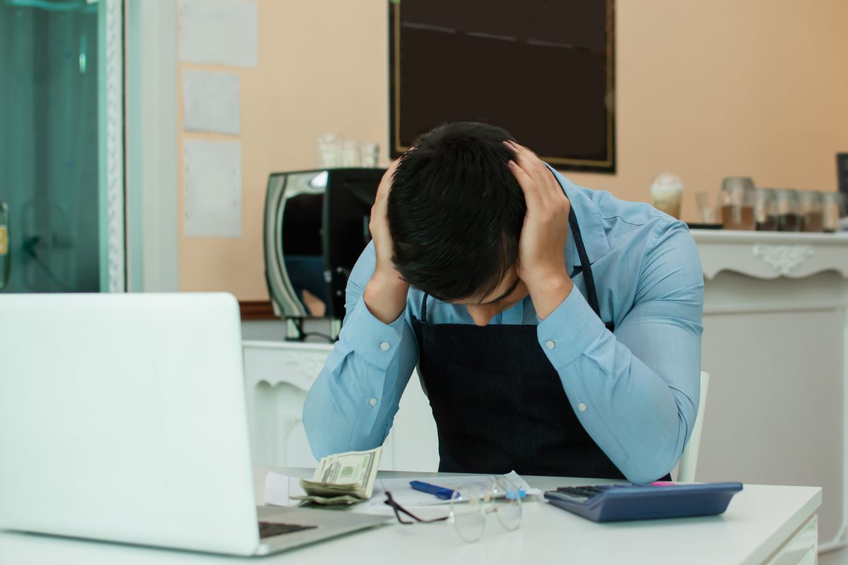 A small business owner holds his head in his hands at a laptop, worried about a fraud investigation